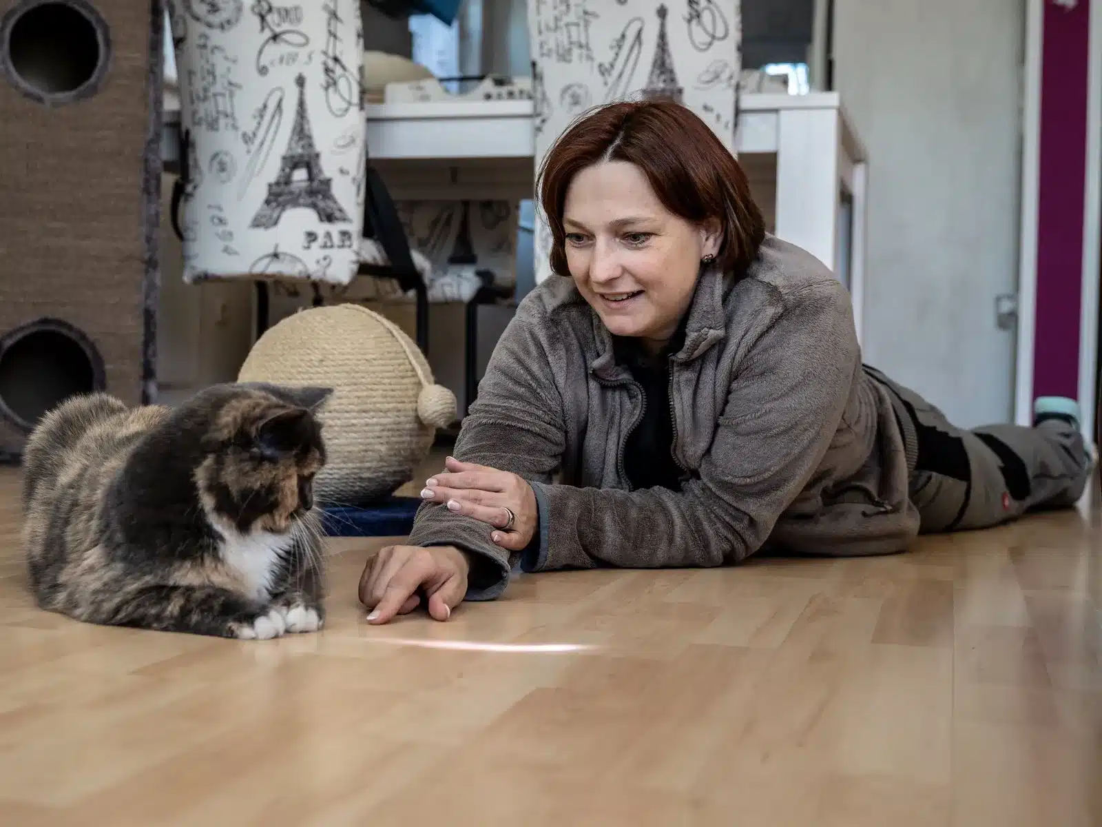 Bianca Wolff liegt auf dem Boden und spielt mit einer Katze während der mobilen Katzenbetreuung.