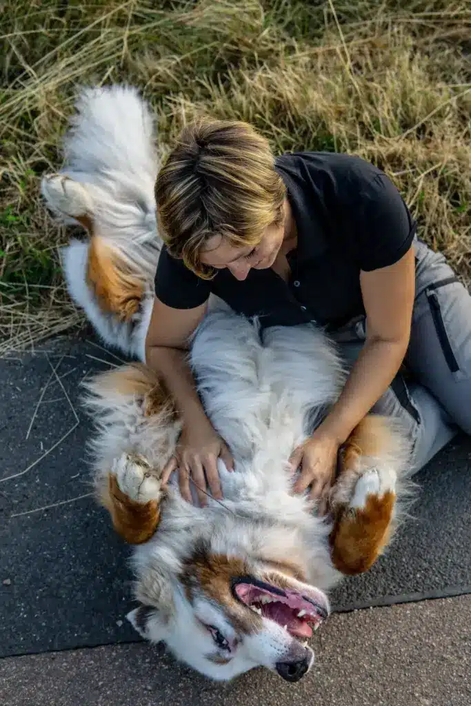 Bianca Wolff sitzt im Gras und kuschelt mit einem weissen Berner Sennenhund mit besonderem Fell.