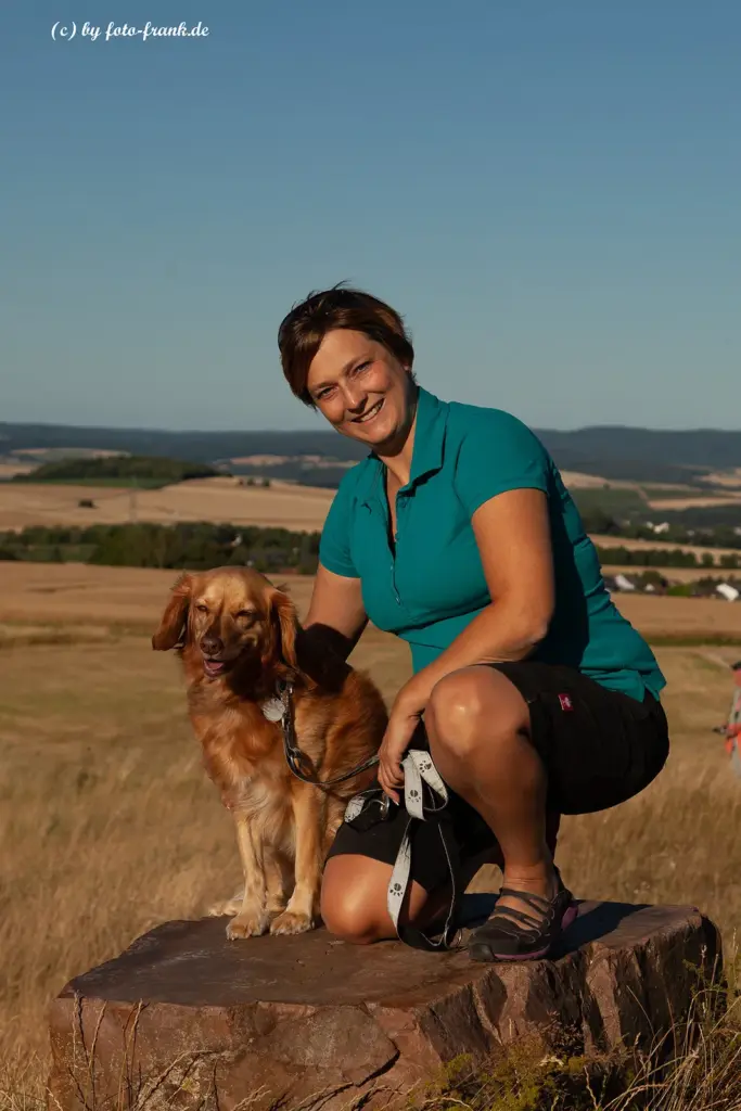 Bianca Wolff steht mit einem Nova Scotia Duck Tolling Retriever im Taunus und blickt mit ihm in die Kamera.
